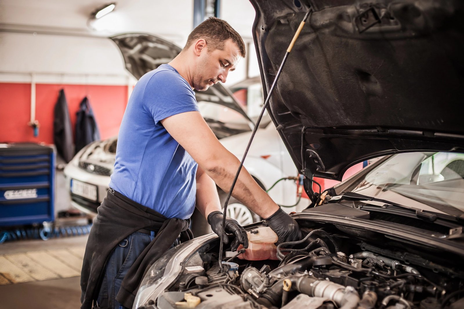 Mechanic in blue shirt working on car engine in auto repair shop, emphasizing trust and expertise in vehicle maintenance.