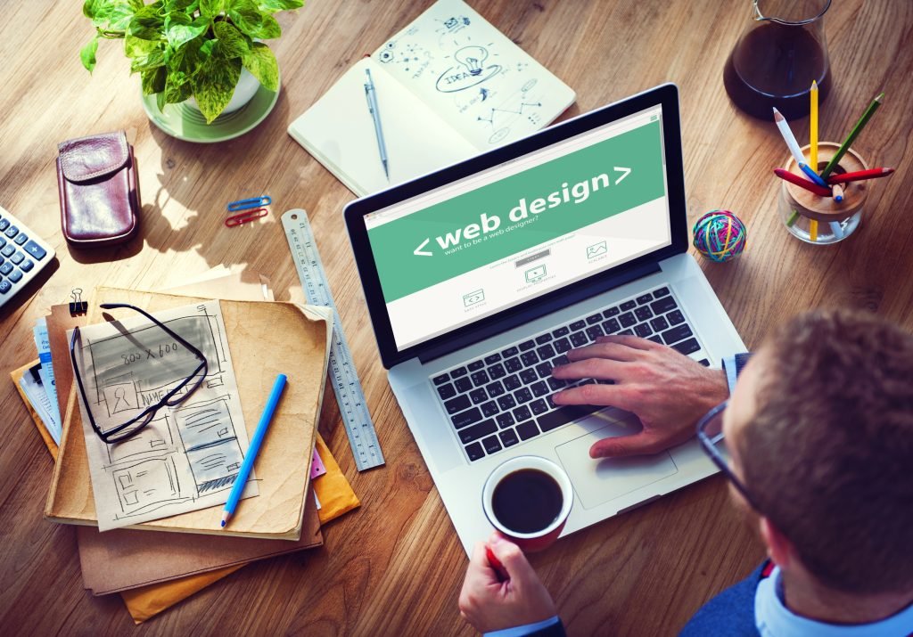 Person working on laptop displaying "web design" webpage, surrounded by design sketches, stationery, and a plant, illustrating digital marketing and website development for local businesses.