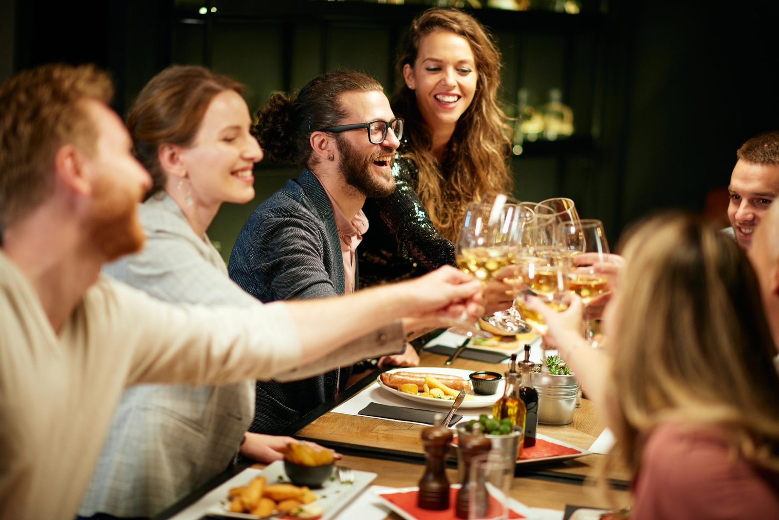 Group of friends toasting with glasses of wine at a dining table, enjoying food and celebrating a memorable experience in a hospitality setting.