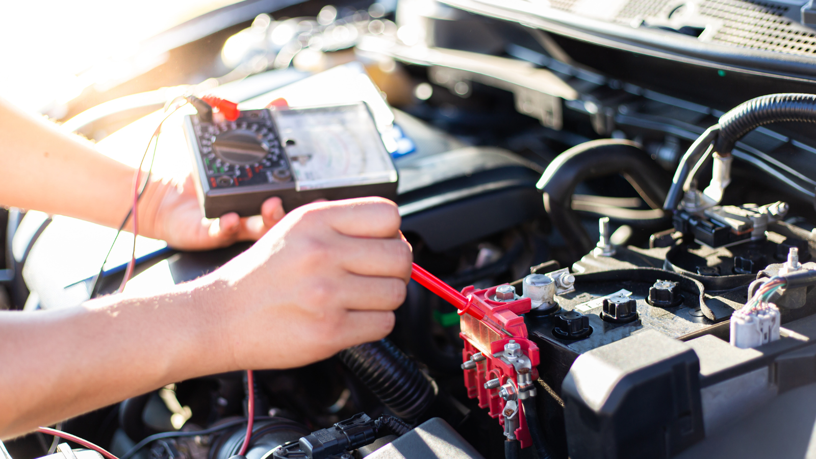 Auto repair technician using a multimeter to test a car battery, illustrating diagnostic work for consistent job quality and performance.