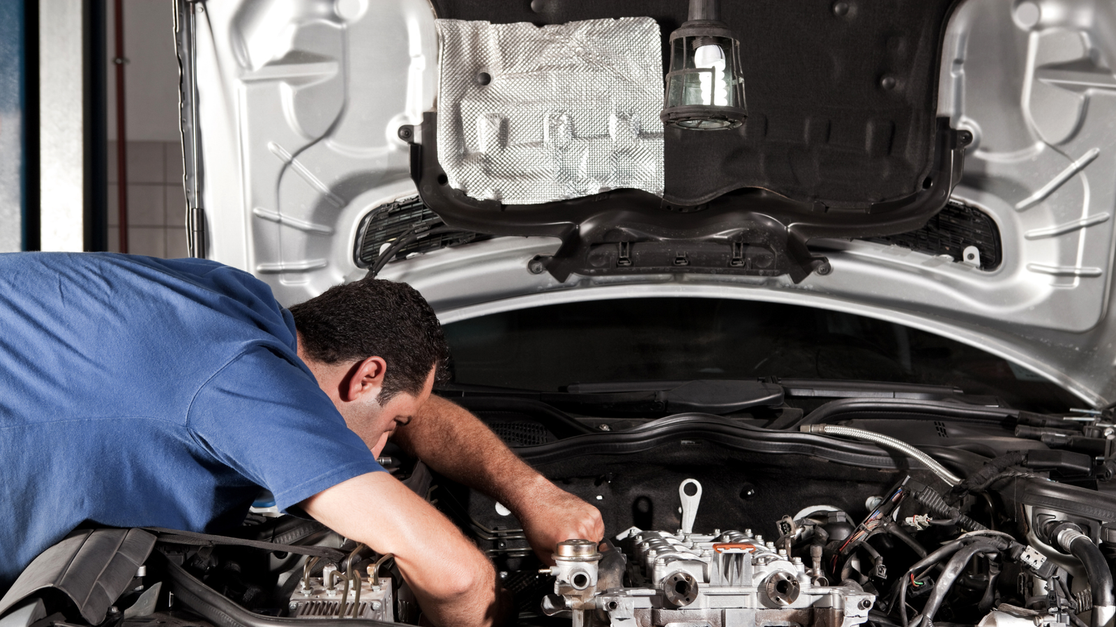 Mechanic working on an auto repair job under the hood of a car, illustrating the hands-on service and expertise relevant to consistent job flow for auto repair shops.