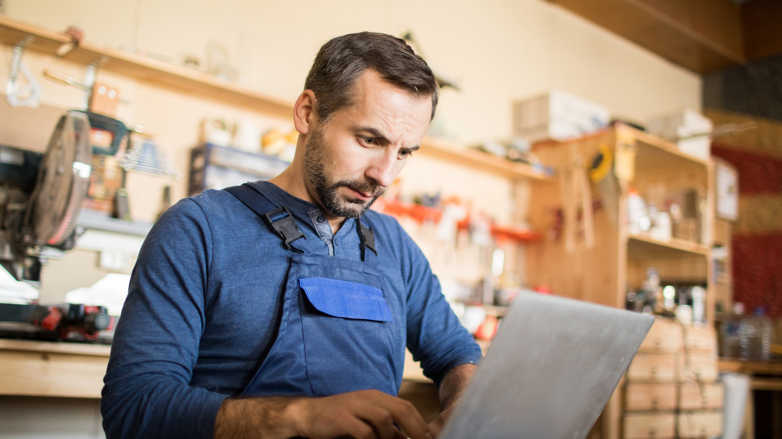 Man in work attire focused on laptop in a workshop, representing small business marketing efforts and digital strategy development for local businesses in Salt Lake City.