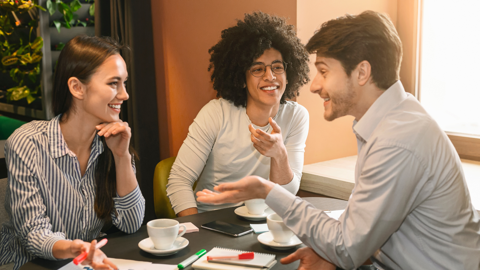 Group of three young professionals engaged in a discussion over coffee, showcasing collaboration and brainstorming for local service business growth strategies.