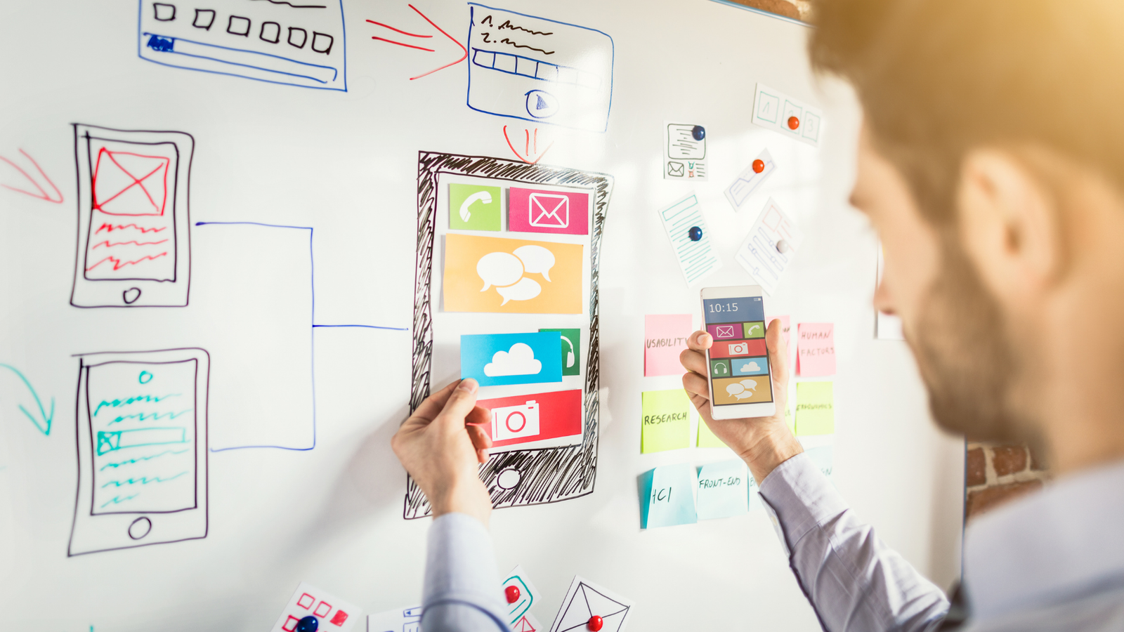 Person interacting with a whiteboard displaying mobile app design elements and colorful icons, emphasizing user experience and digital strategy for local service businesses.