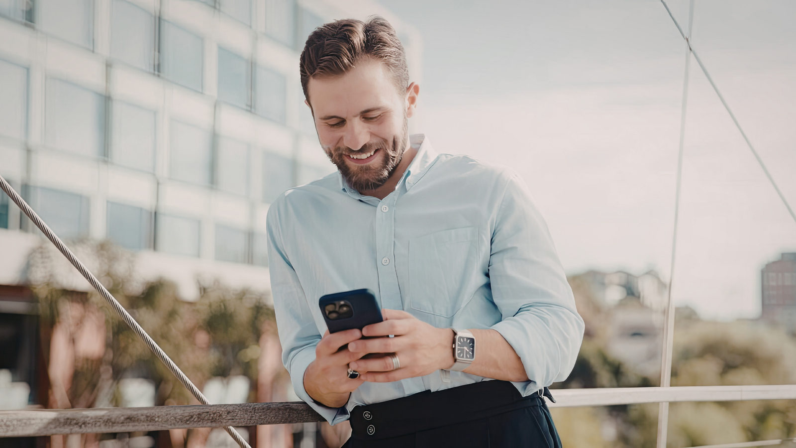 Smiling man in a light blue shirt using a smartphone, representing engagement and modern communication for local service businesses.