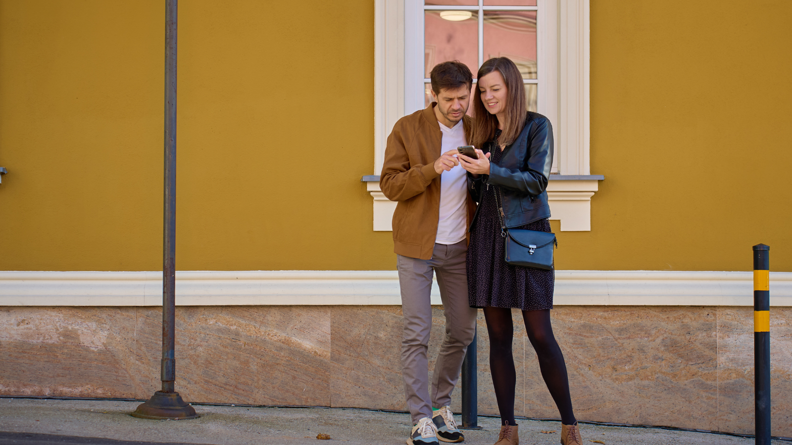 Couple looking at smartphone together, standing against a yellow wall, illustrating user engagement and digital interaction for local service businesses.