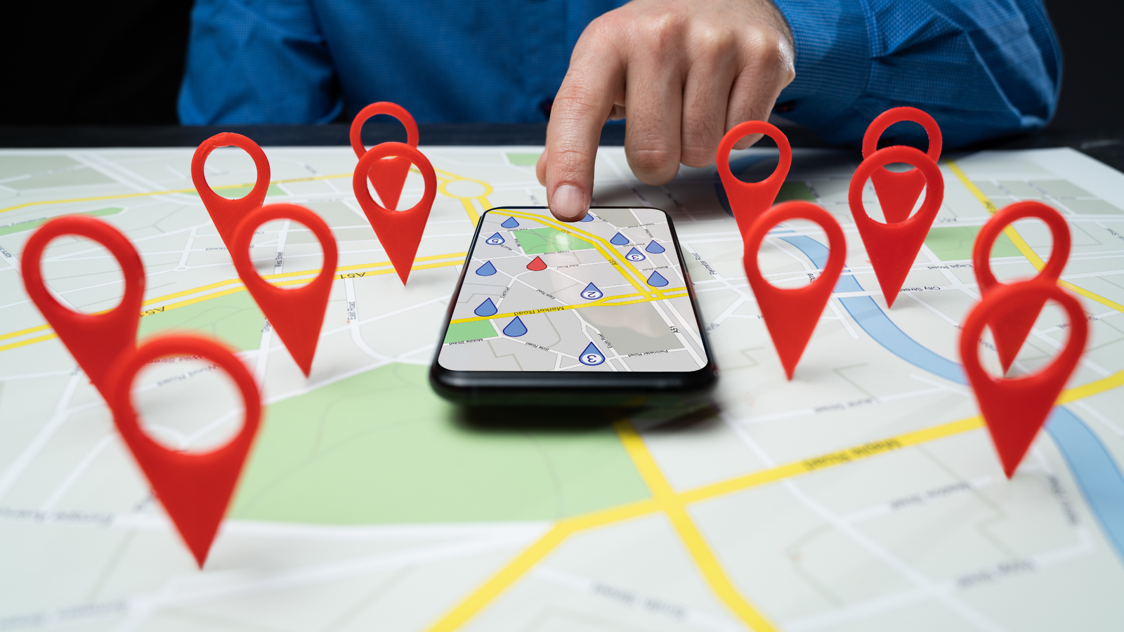 Hand pointing at smartphone displaying a map with multiple red location pins, illustrating local SEO visibility and Google Maps optimization for businesses.