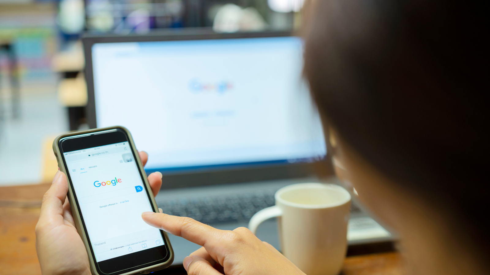 Person using smartphone to search Google, with laptop in background, emphasizing local SEO and online visibility for businesses.