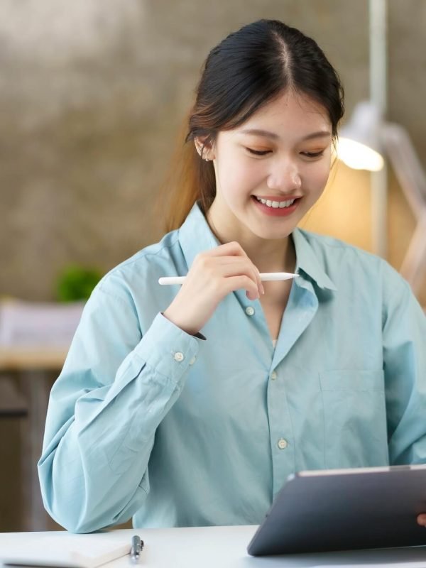 Young Asian businesswoman using a digital tablet in an office setting, smiling and holding a stylus, representing marketing strategy and digital solutions for local businesses.
